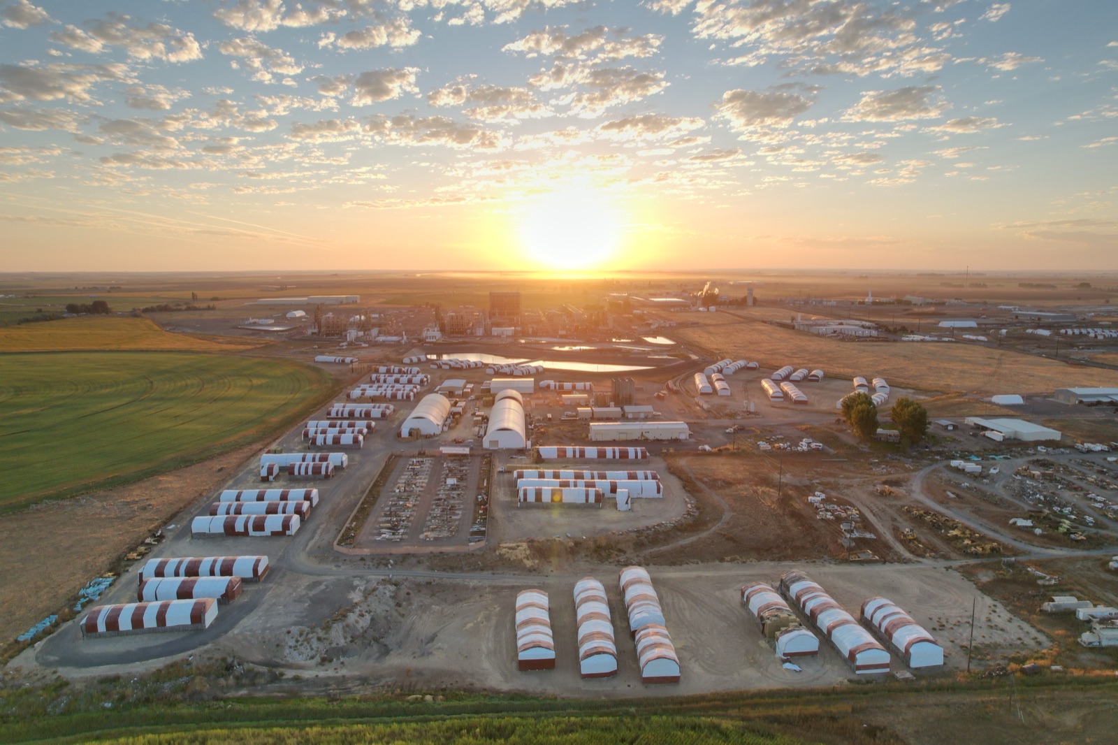 Aerial view of the Courtright Enterprises hay export facility at sunset, with rows of red-and-white striped press barns across the Columbia Basin
